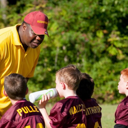 Coach talking to group of young athletes in maroon jerseys