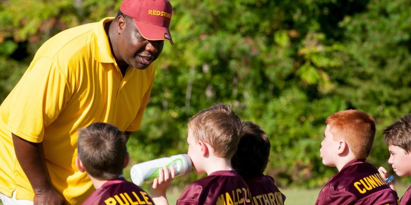 Coach talking to group of young athletes in maroon jerseys