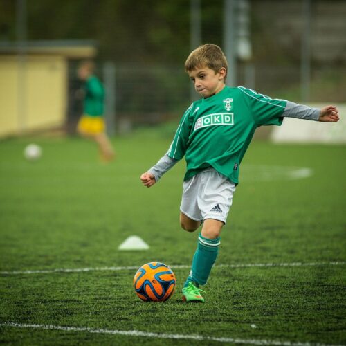 Child kicking orange soccer ball on athletic field