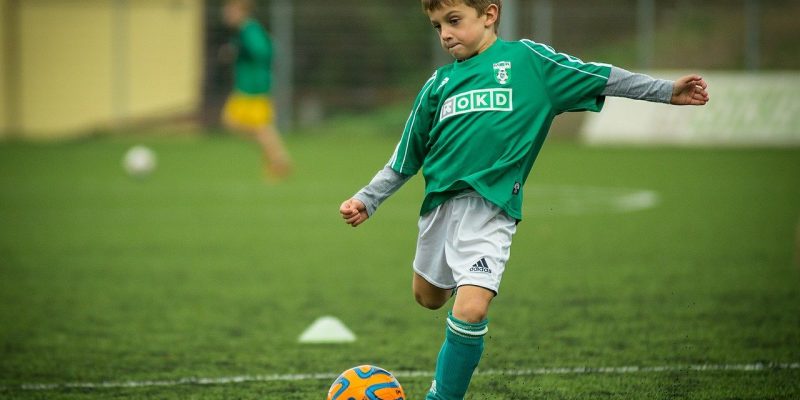 Child kicking orange soccer ball on athletic field