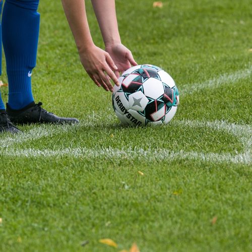 Person reaching down to pick up soccer ball on grassy field