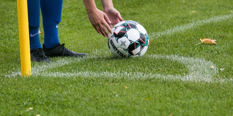 Person reaching down to pick up soccer ball on grassy field