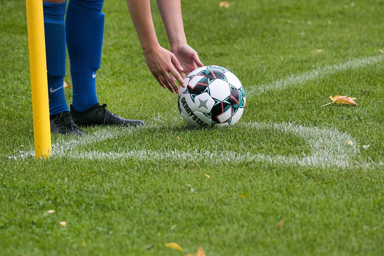 Person reaching down to pick up soccer ball on grassy field