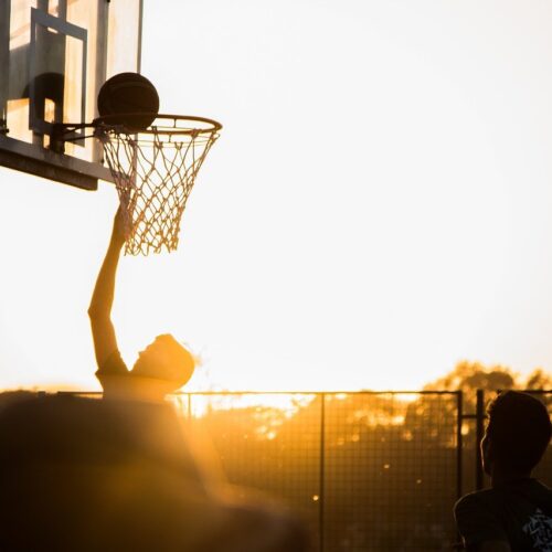 Teenager playing basketball at sunset