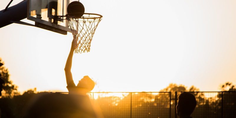 Teenager playing basketball at sunset