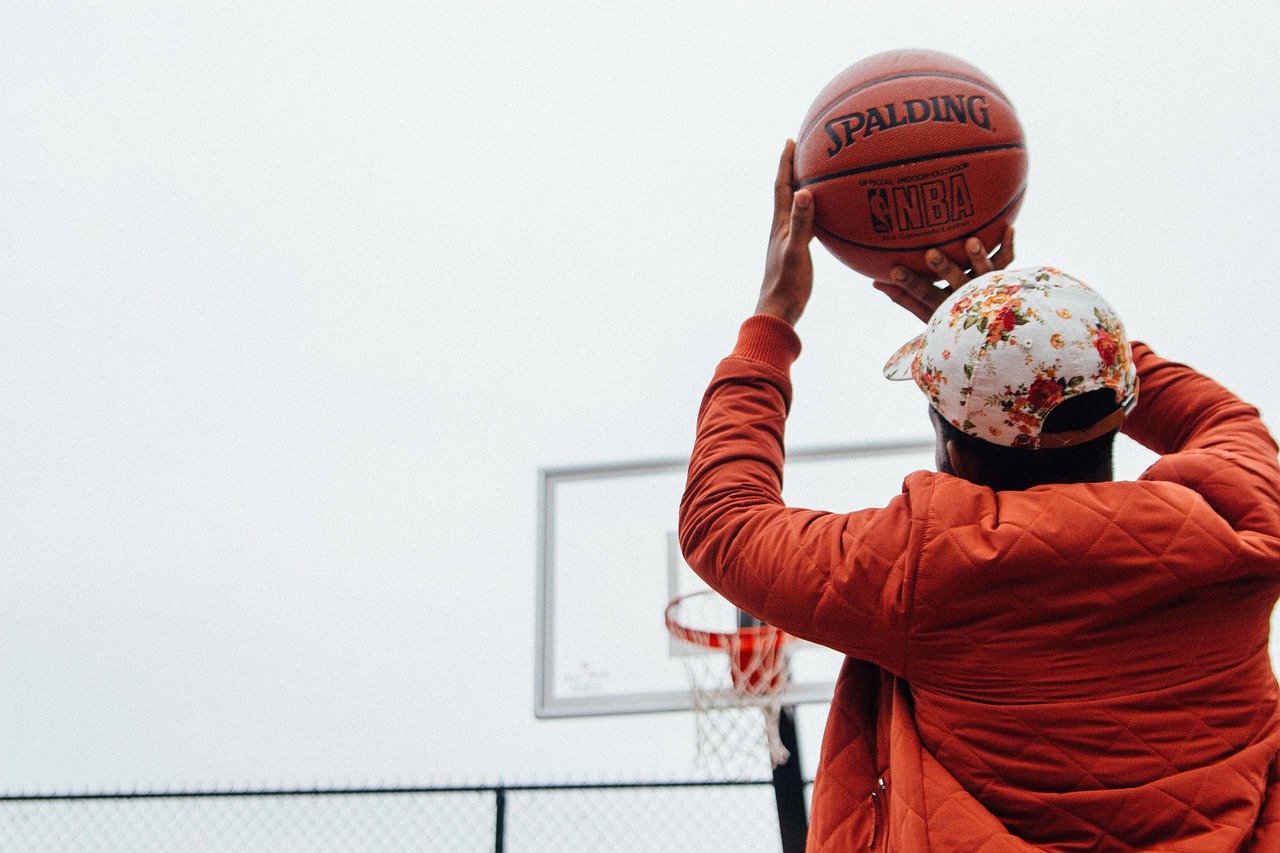 Teenager in orange jacket shooting basketball at hoop