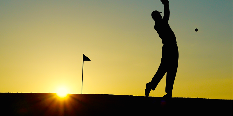 Silhouette of man playing golf at sunset on course