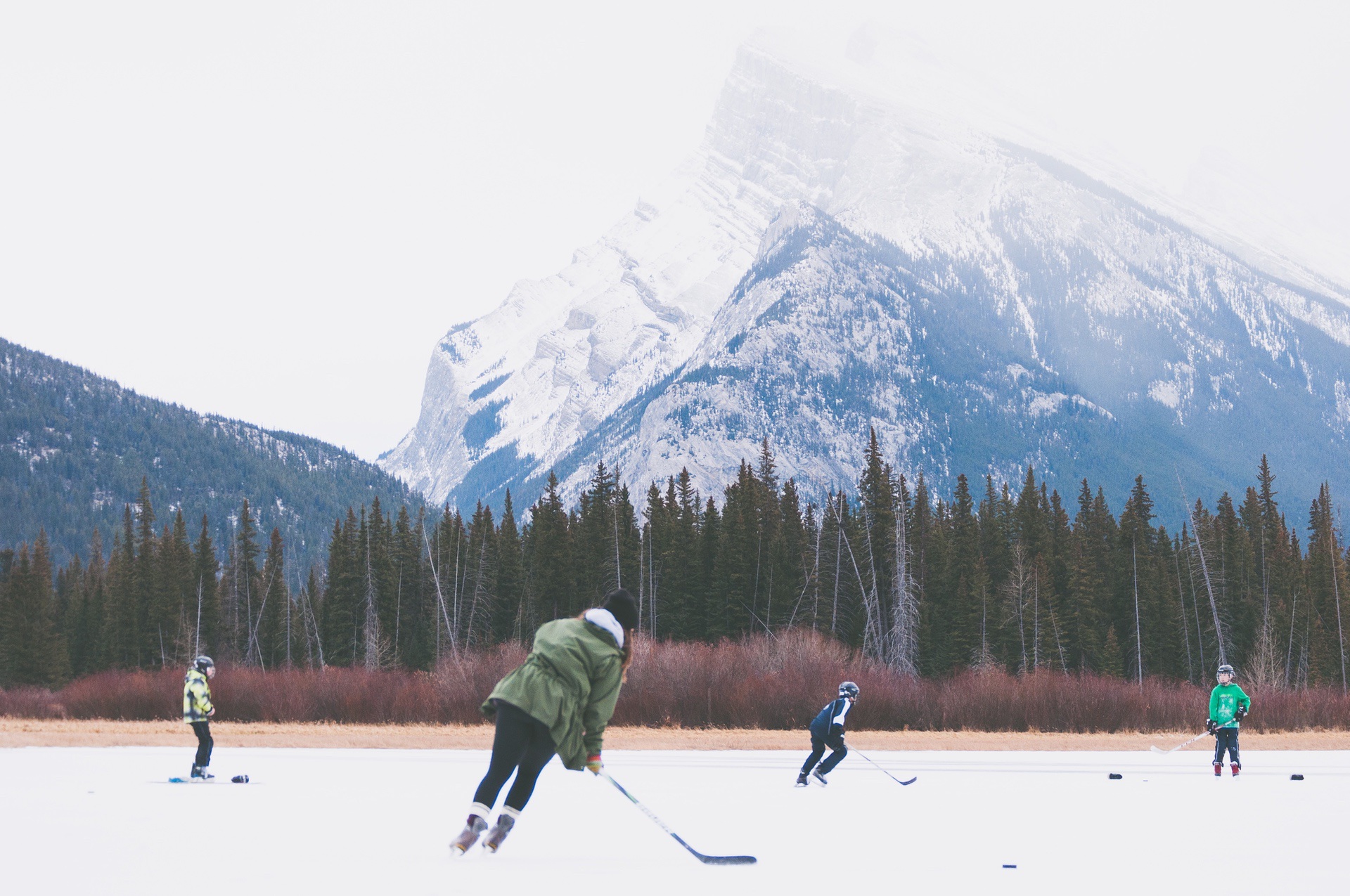 Group of youths playing hockey on frozen lake near mountains