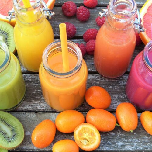 Various smoothies in jars on table next to assorted fruits