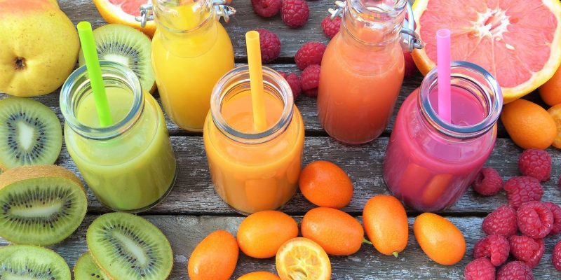 Various smoothies in jars on table next to assorted fruits